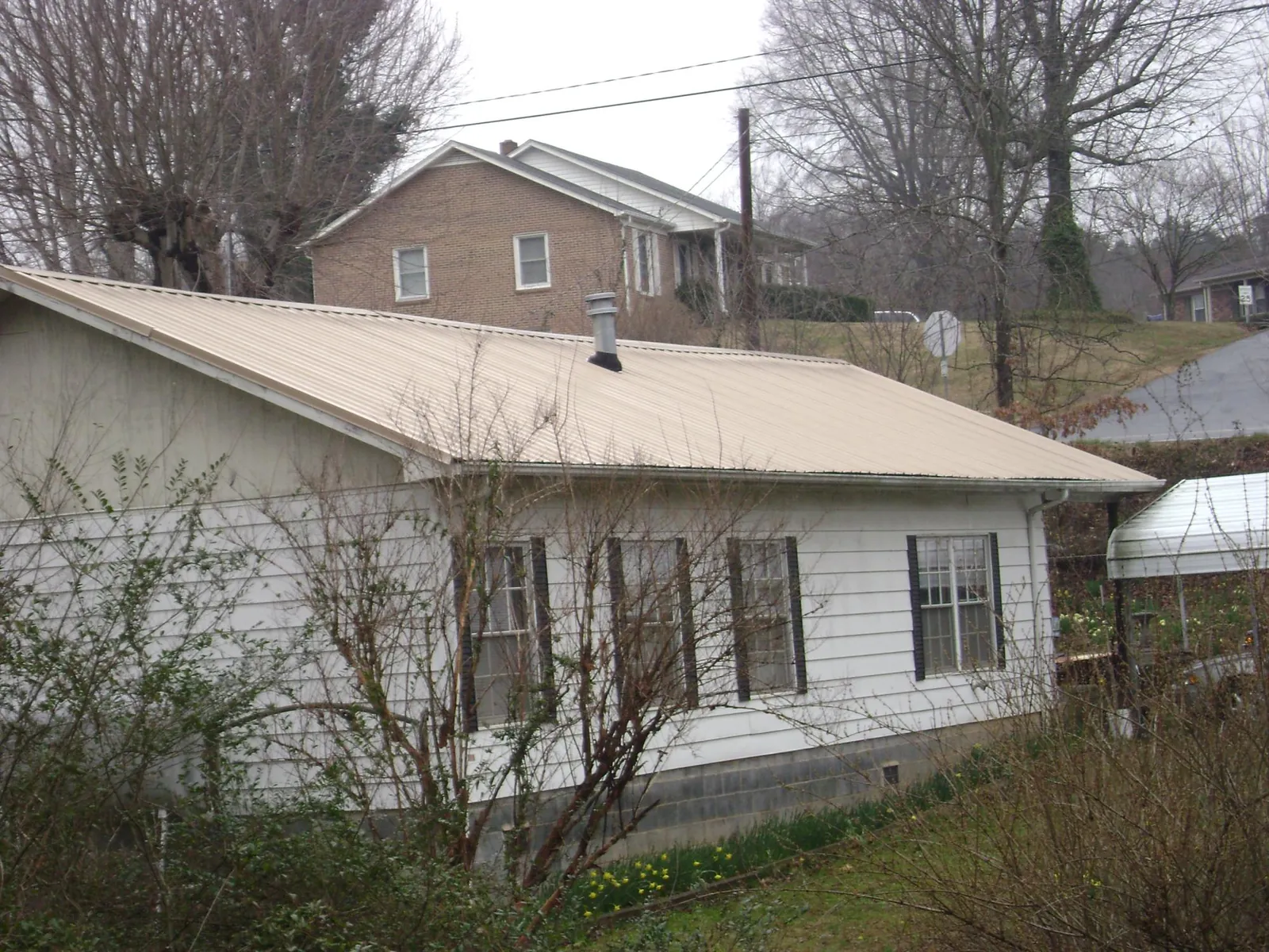 Tan metal roof on a white sided house set into a hillside — Commercial Roofing by Roofing Brothers in Hyattsville